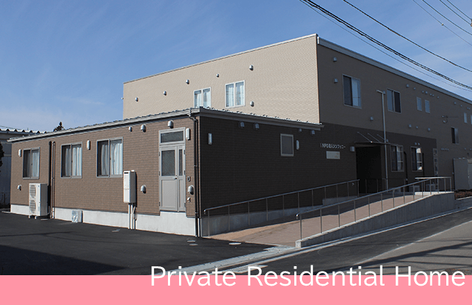 介護施設の建物外観。レンガ造りで複数棟からなる施設。前面に駐車スペースと階段がある。